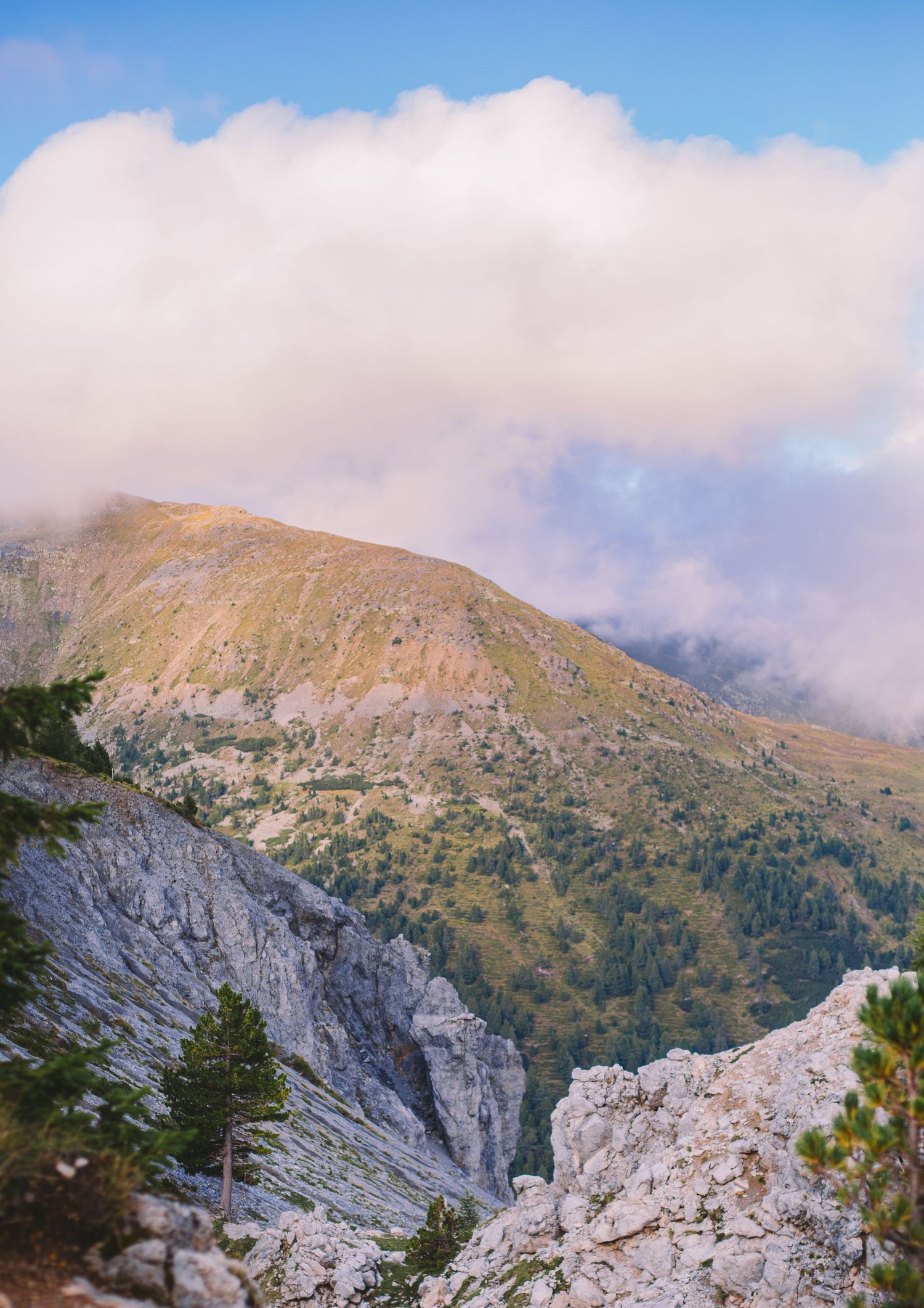 Rocky mountain terrain with steep cliffs and vegetation under cloudy skies.