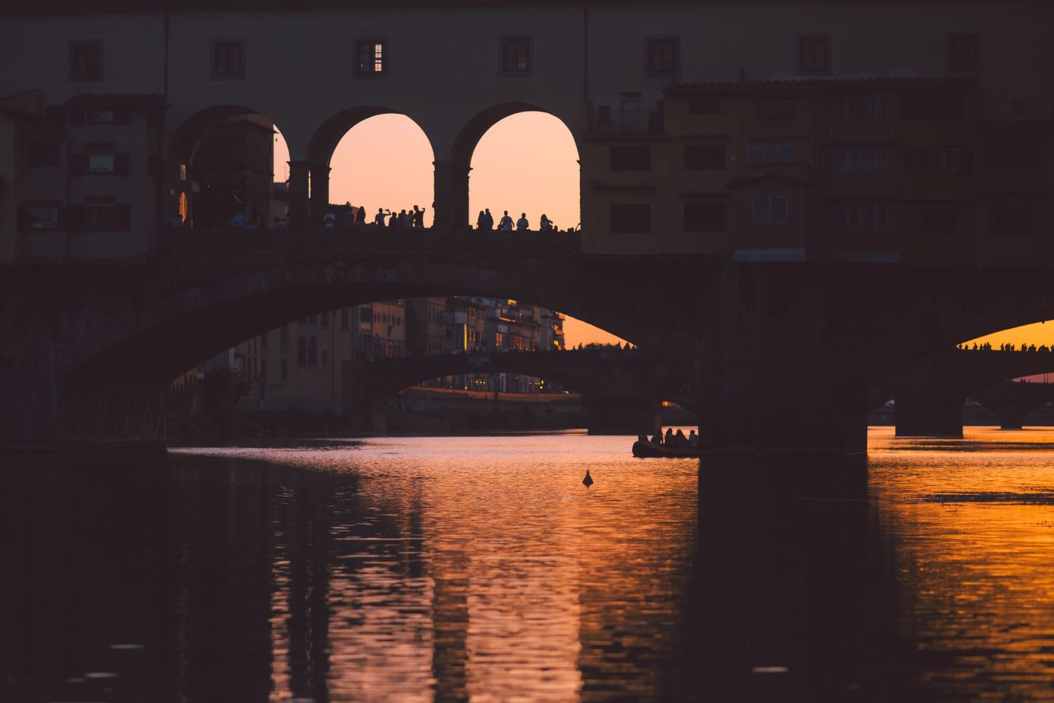 Silhouette of stone bridge arches reflecting on calm water at sunset.