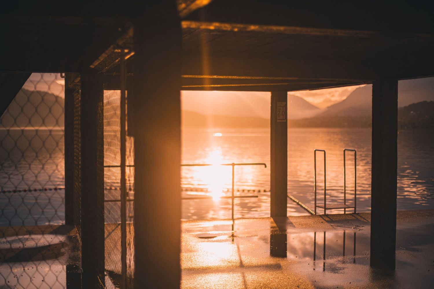 Sunset view through indoor pillars overlooking a waterfront with golden reflections.