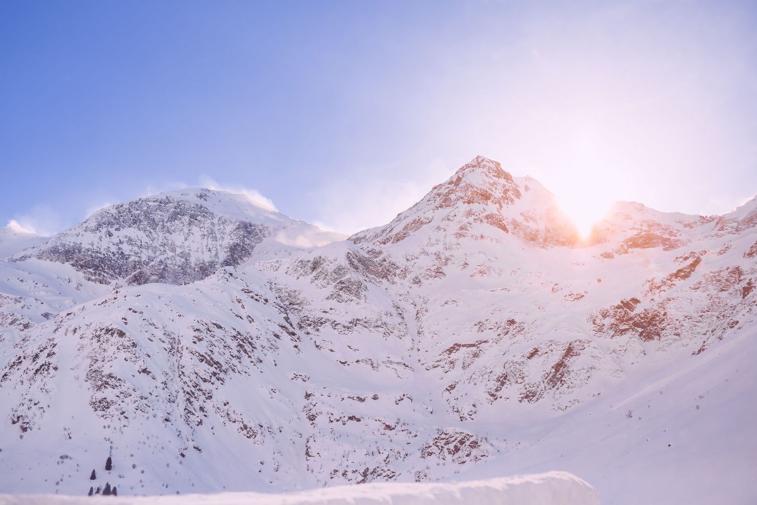 Snow-covered mountain peaks glowing in pink sunlight against blue sky.