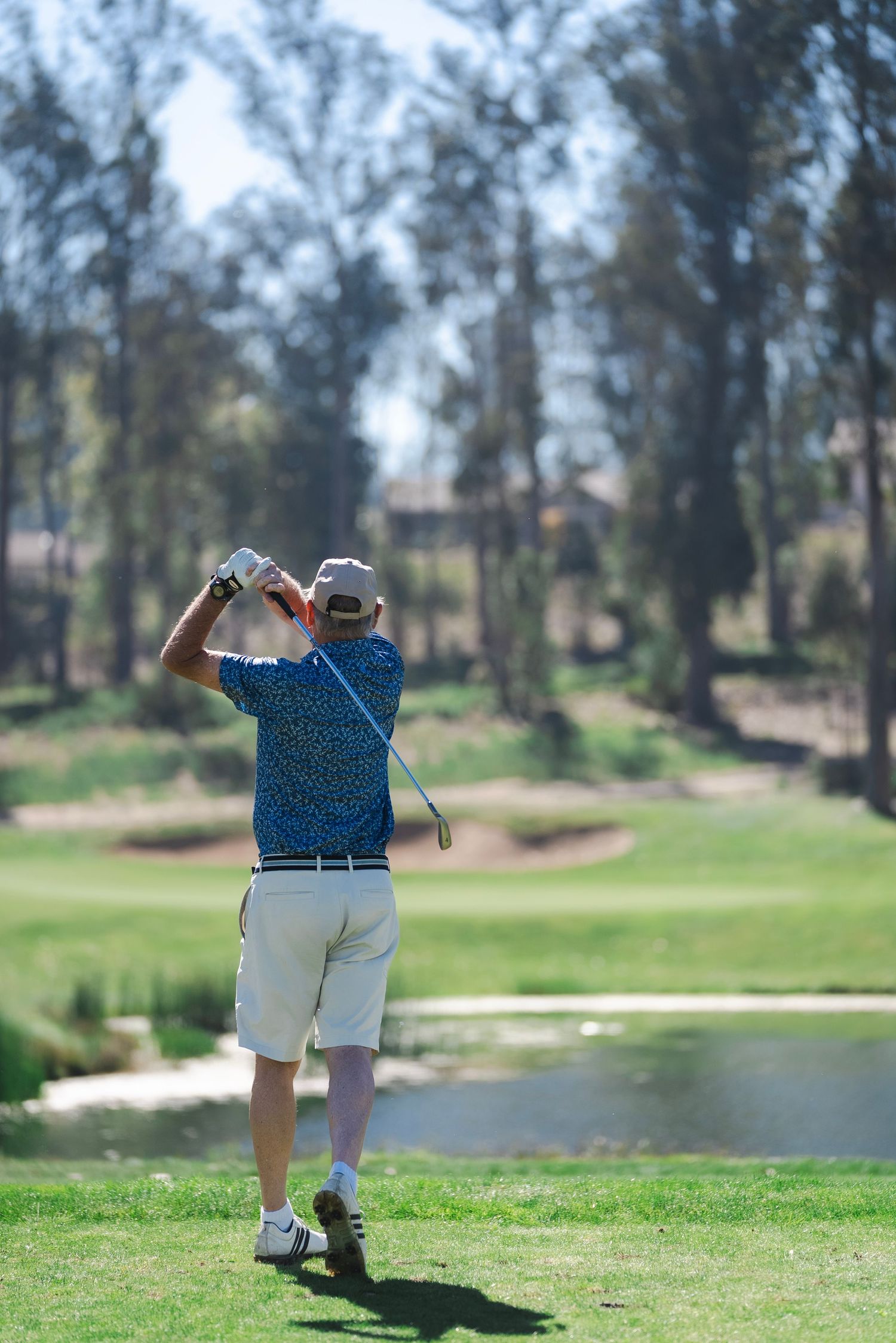 A man swings a club and hits a golf ball at a course on a sunny day.