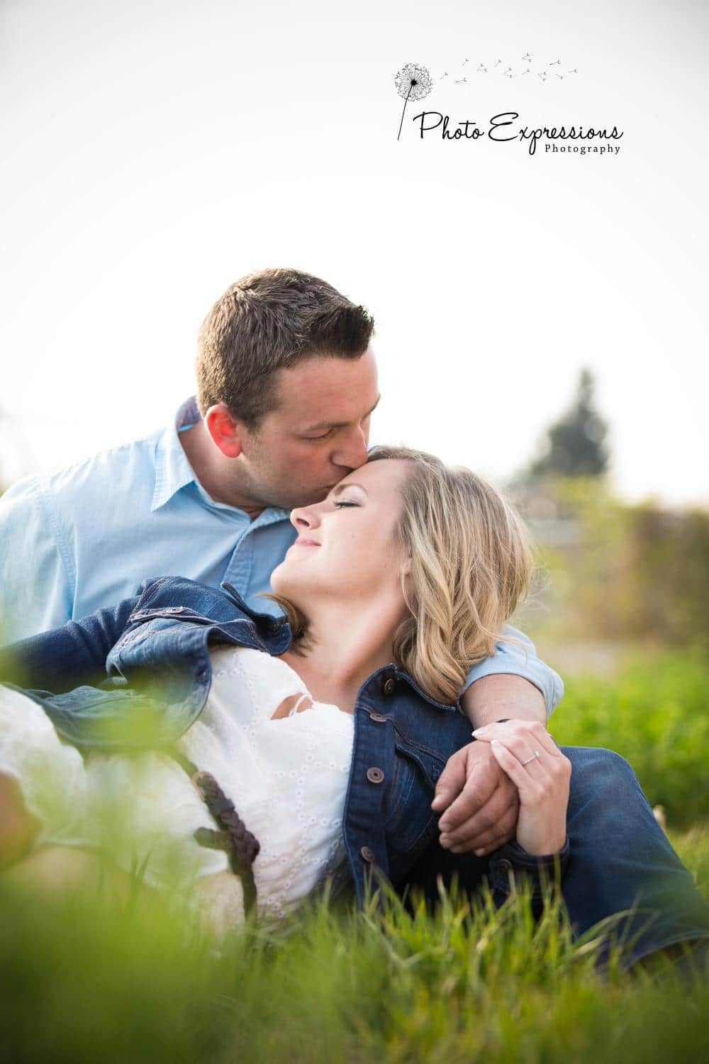 Couple lying in green grass sharing romantic moments during outdoor photoshoot.