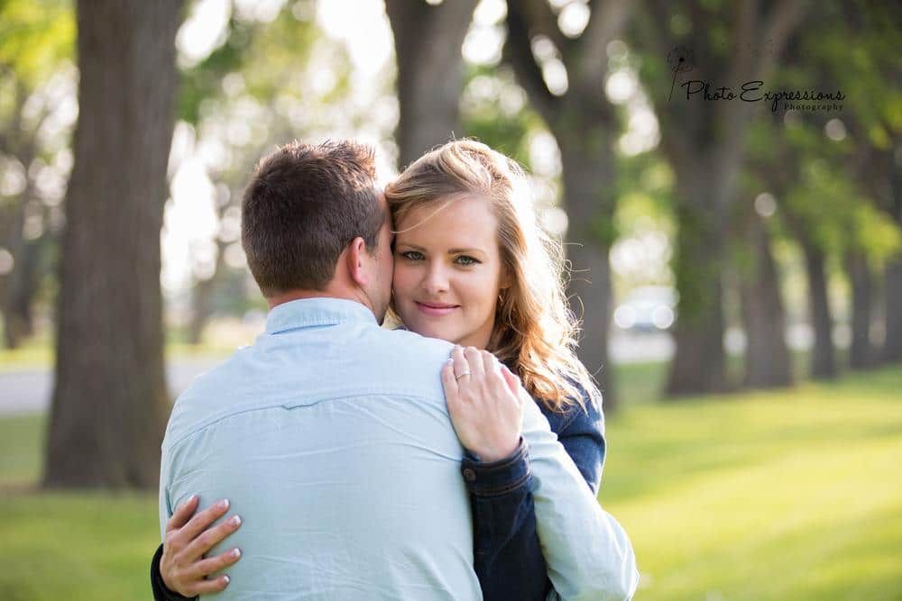Couple embracing in sunny park setting with trees in background.