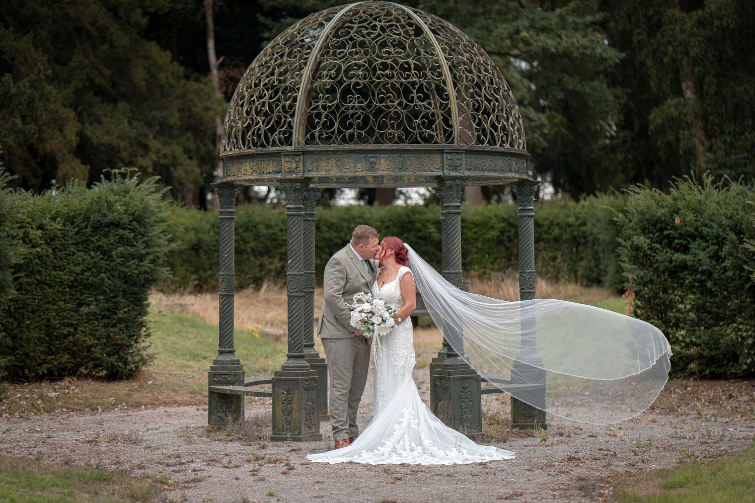 Romantic wedding portrait under an ornate metal gazebo with flowing veil.