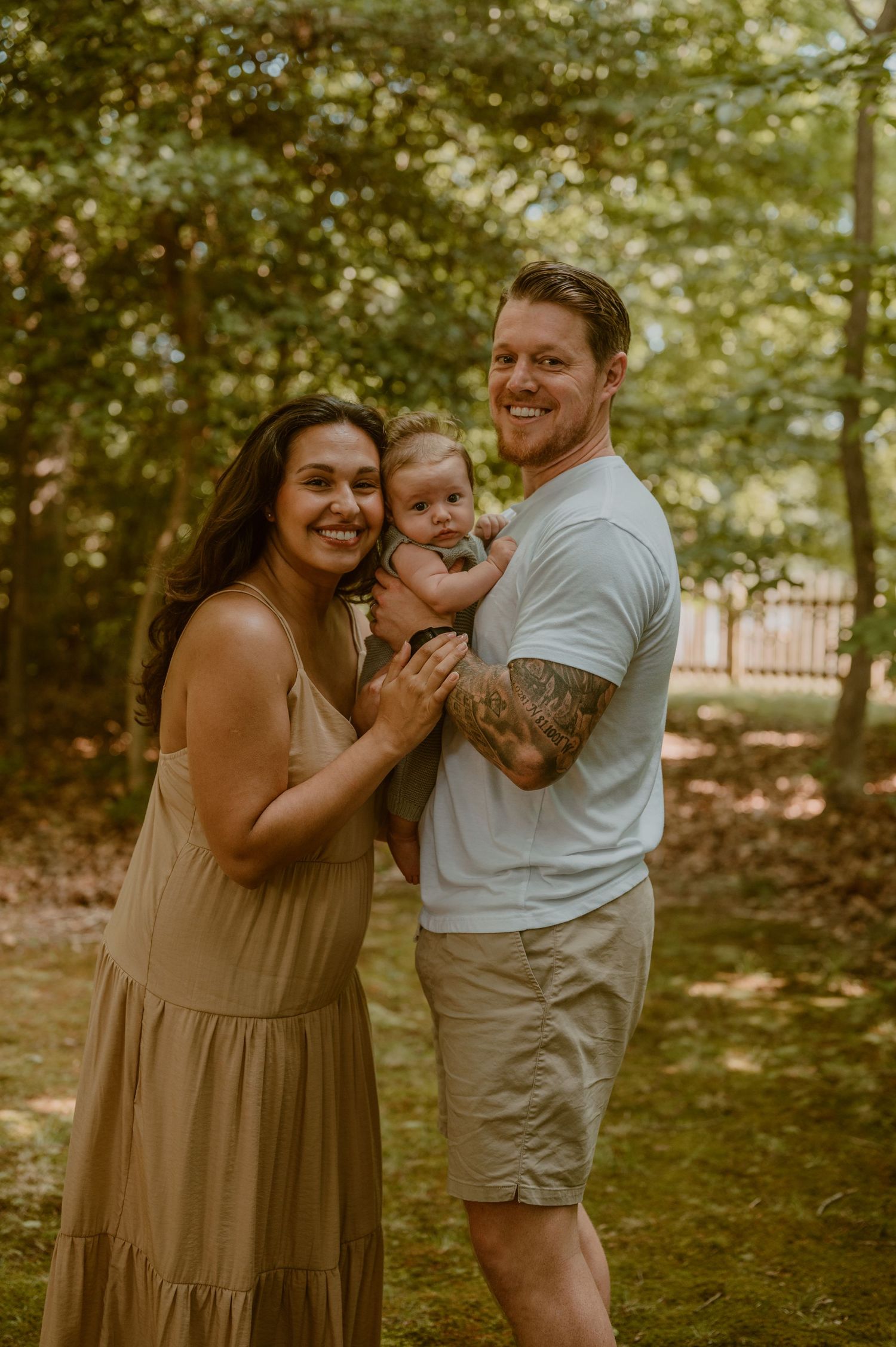 A family shares a joyful moment together in a sunlit wooded area during a summer photo session by Samantha Campbell imagery