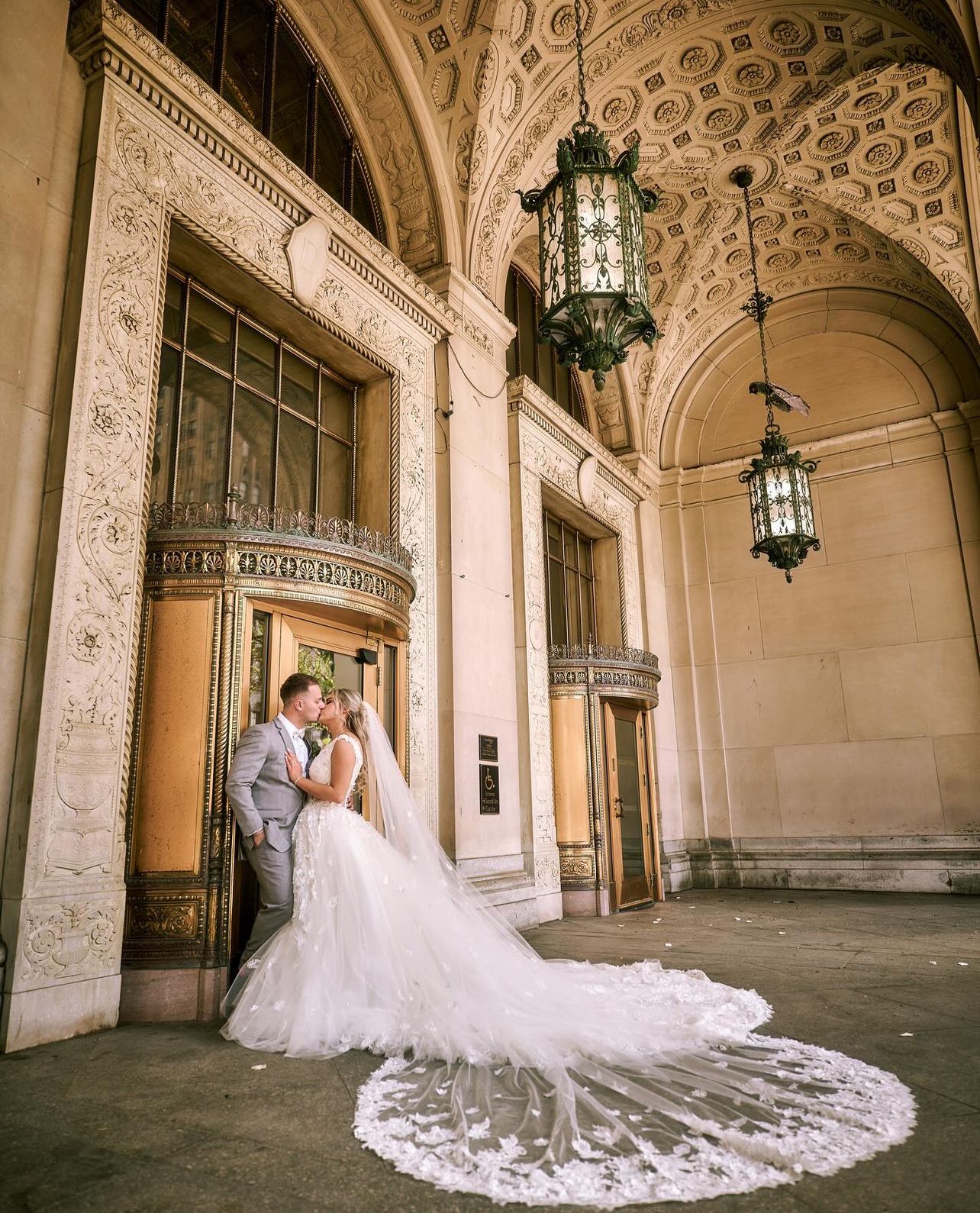 Wedding portrait under ornate stone archway with flowing lace train.