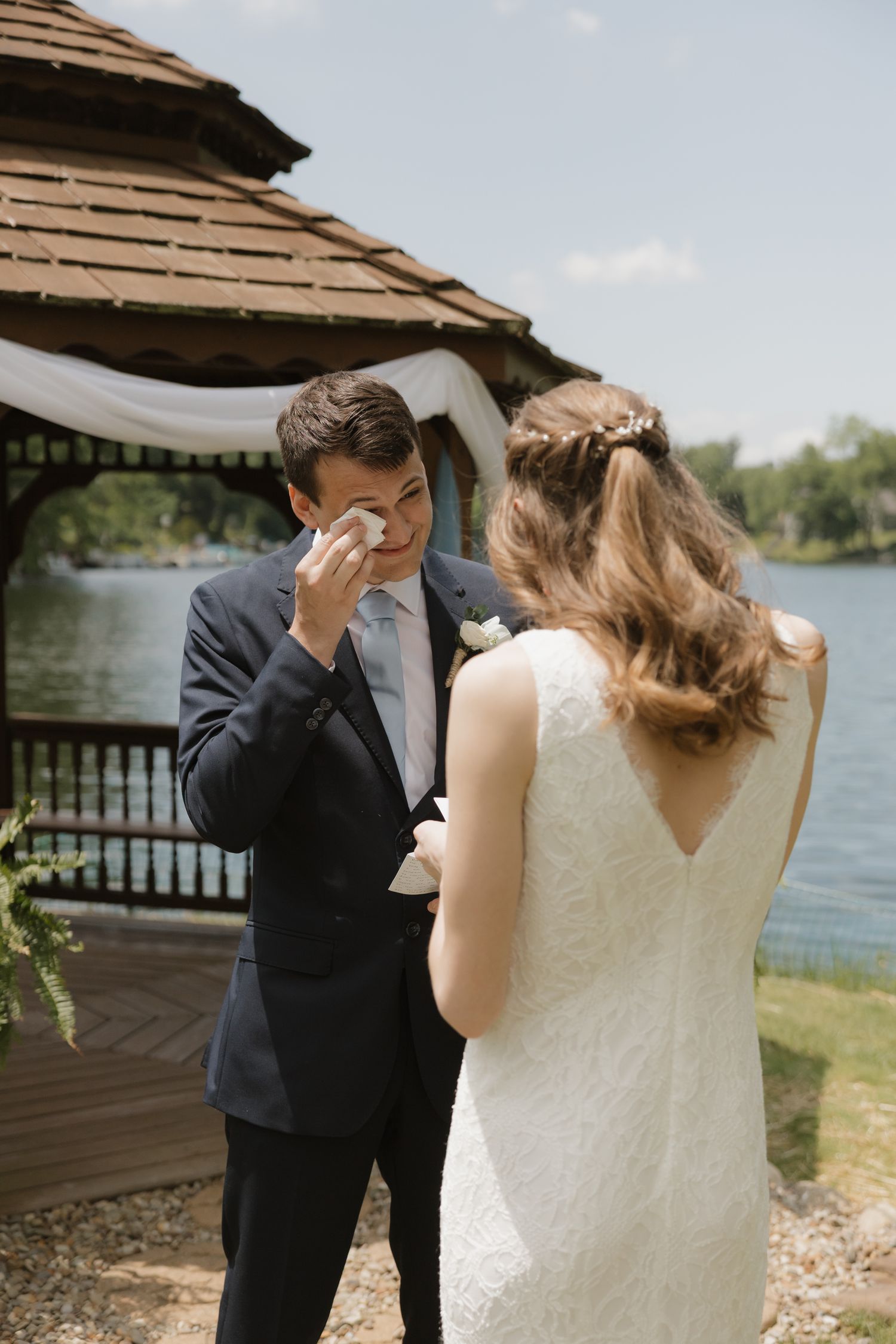 A couple shares an emotional first look moment at their lakeside wedding under a gazebo.
