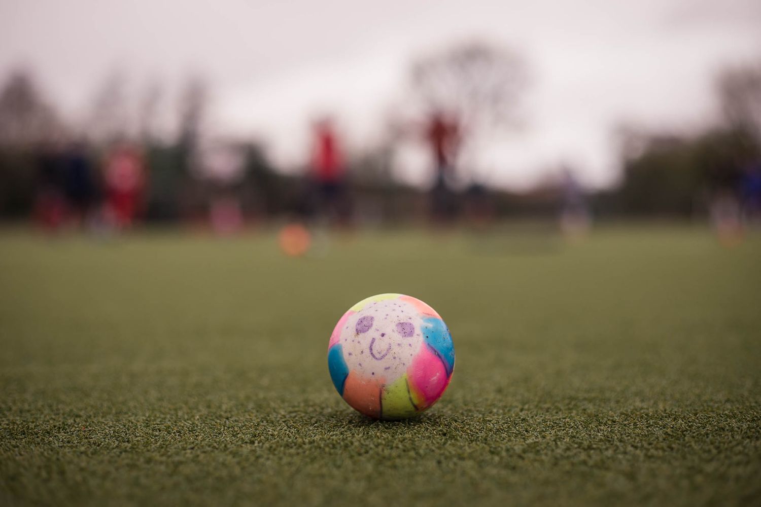 Smiley face drawn on a hockey ball with blurred players in the background at Redditch Hockey Club