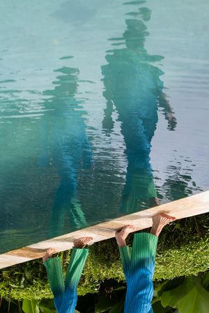 Reflection in turquoise water shows silhouettes against vibrant blue and green tones.