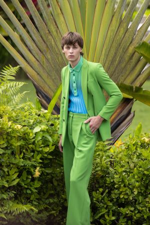 Person in bright green suit and blue shirt posing against large tropical palm frond.