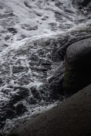 Close-up of ocean waves crashing against dark rocky shore.