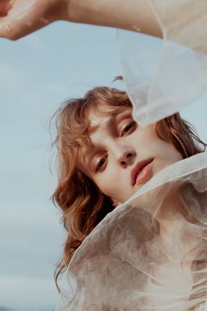 Artistic beauty portrait through flowing sheer fabric with natural lighting.