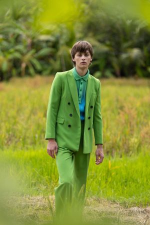 Person wearing vibrant lime green suit standing in tropical field.