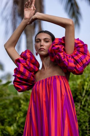 Vibrant fuchsia and orange ruffled gown with dramatic puff sleeves in a tropical setting.