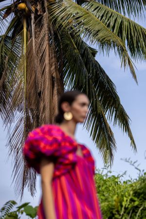 Pink ruffled dress photographed against a tropical palm tree backdrop.