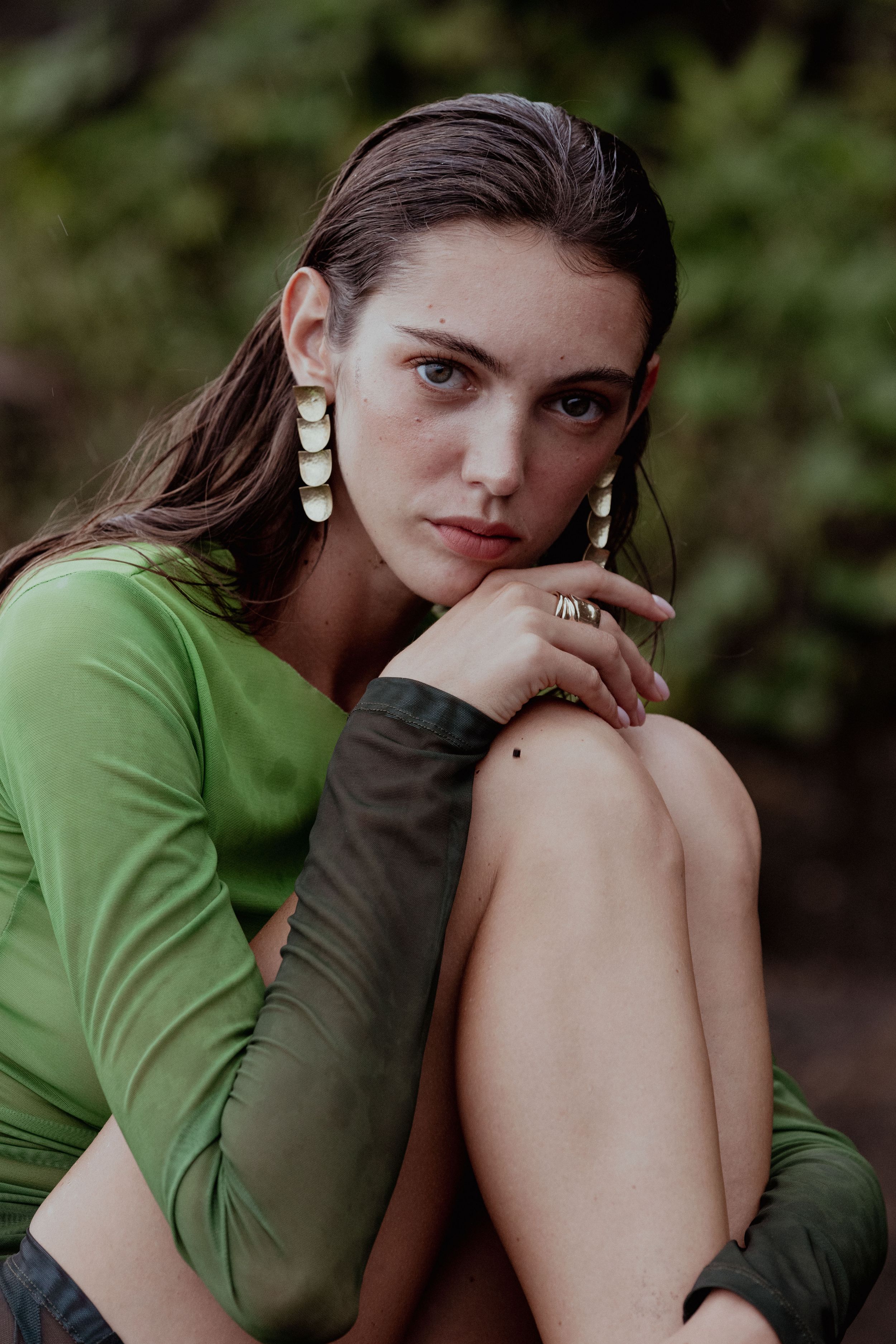 Portrait in natural lighting wearing green long sleeve top and statement earrings.