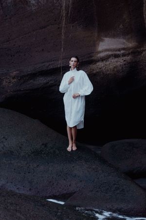 Ethereal fashion scene with white dress against dark rocky landscape.