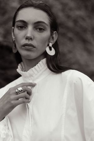 Monochrome fashion portrait with dramatic white blouse and circular statement earrings.