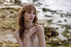 Ethereal portrait of model in neutral tones against rocky coastal background.