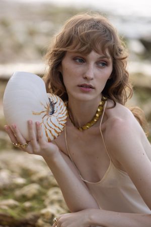 Artistic fashion photo featuring model holding decorative shell with gold details.