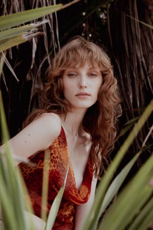 Portrait in tropical setting with model wearing red patterned dress among palm fronds.