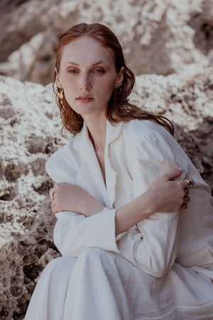 Romantic portrait in flowing white dress against textured stone backdrop.