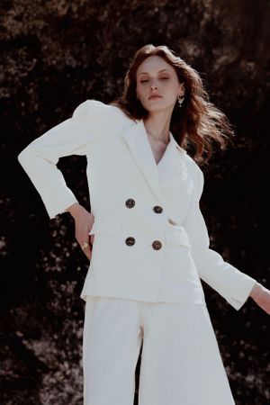 Model wearing crisp white double-breasted suit against dark textured background.