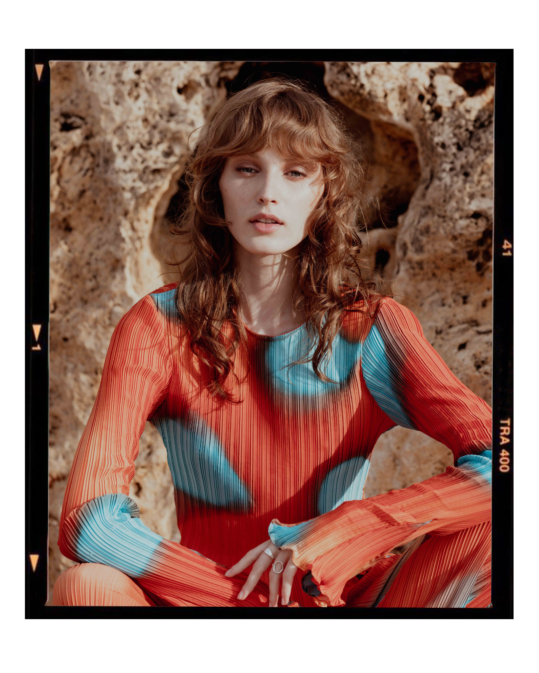 Retro-styled portrait in coral and turquoise pleated dress against stone backdrop.