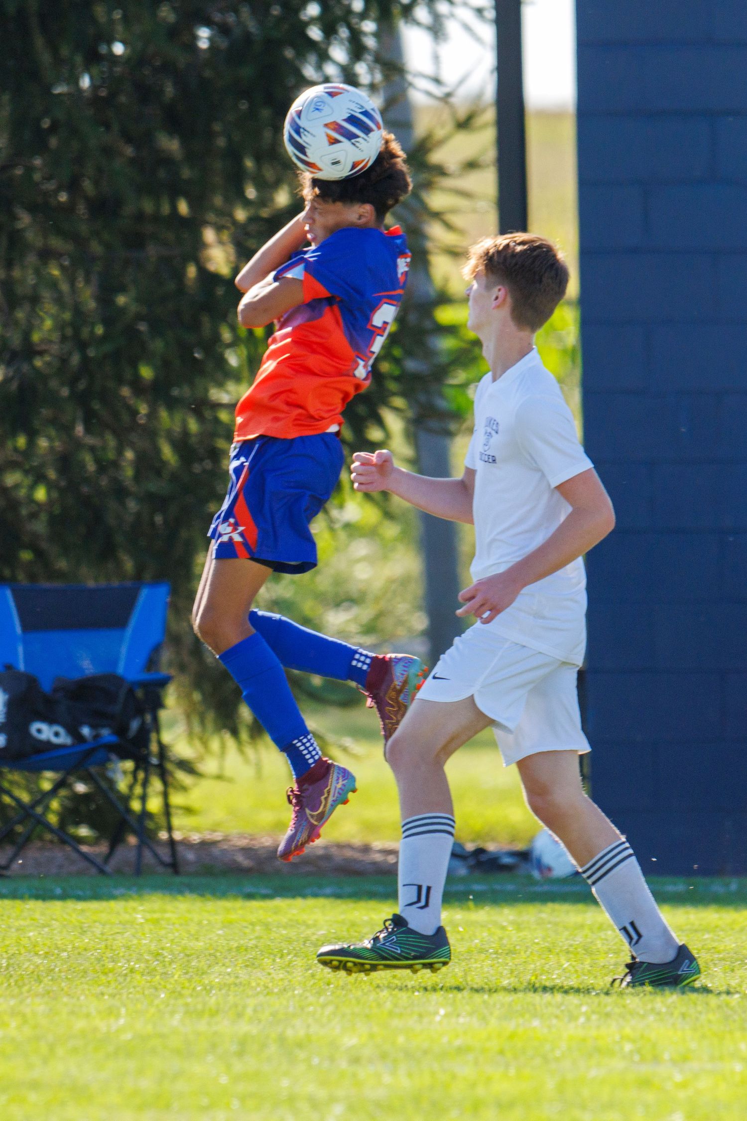 Soccer players in orange and white uniforms compete for ball control during an outdoor match on grass field.