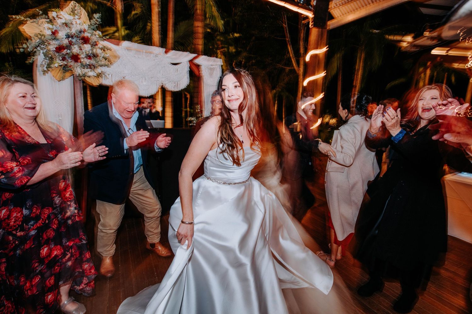 A bride in a satin gown dances with guests during the wedding reception.