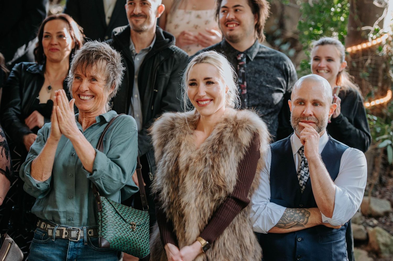 Wedding guests react emotionally during ceremony in outdoor forest setting.