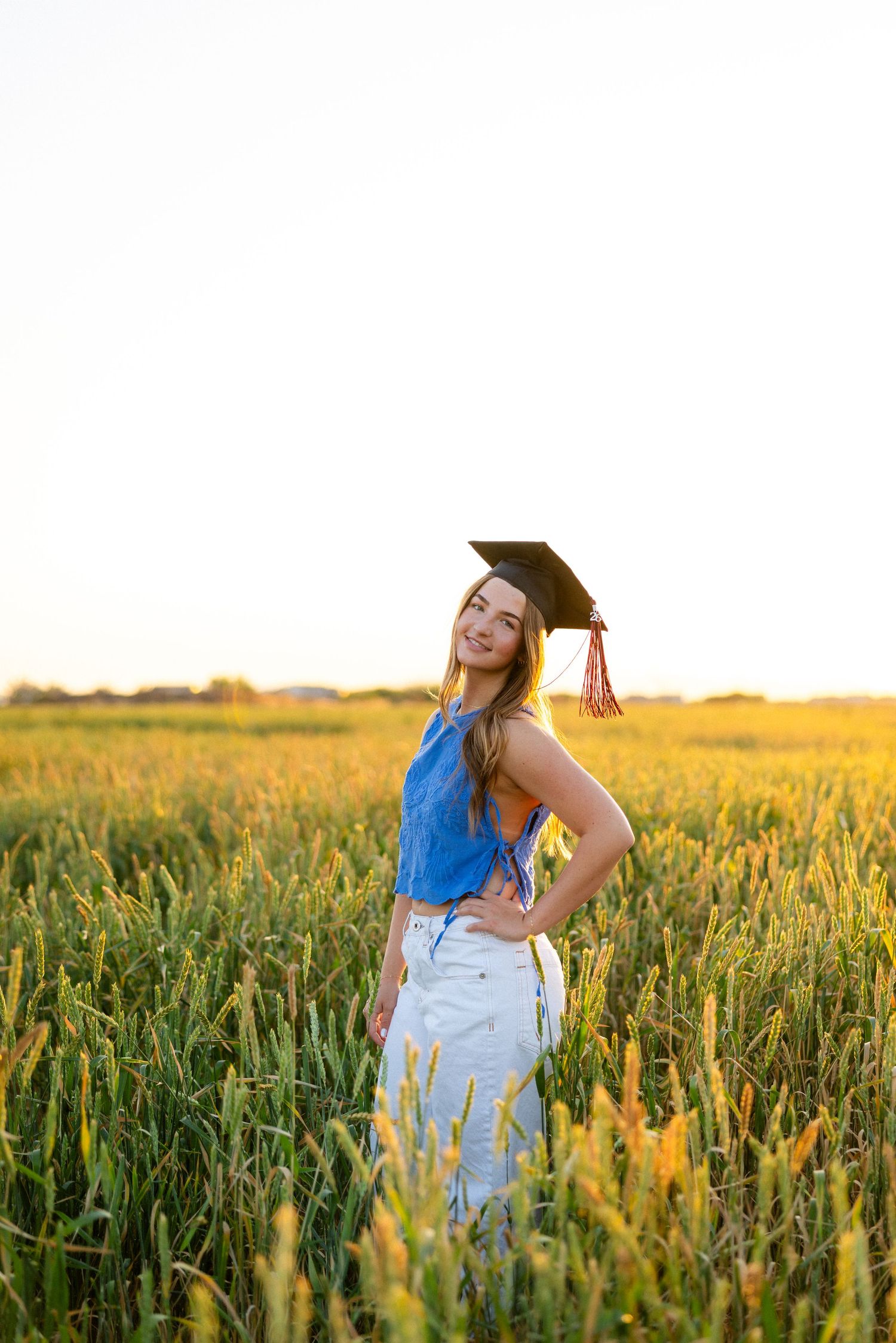 Graduate in cap and gown stands by wooden fence in desert landscape with saguaro cactus and golden sunset.