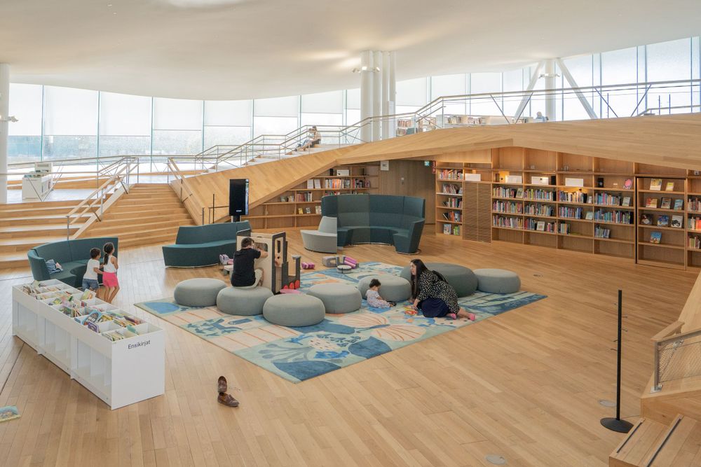 Contemporary library lounge area with comfortable seating and blue carpet surrounded by bookshelves.