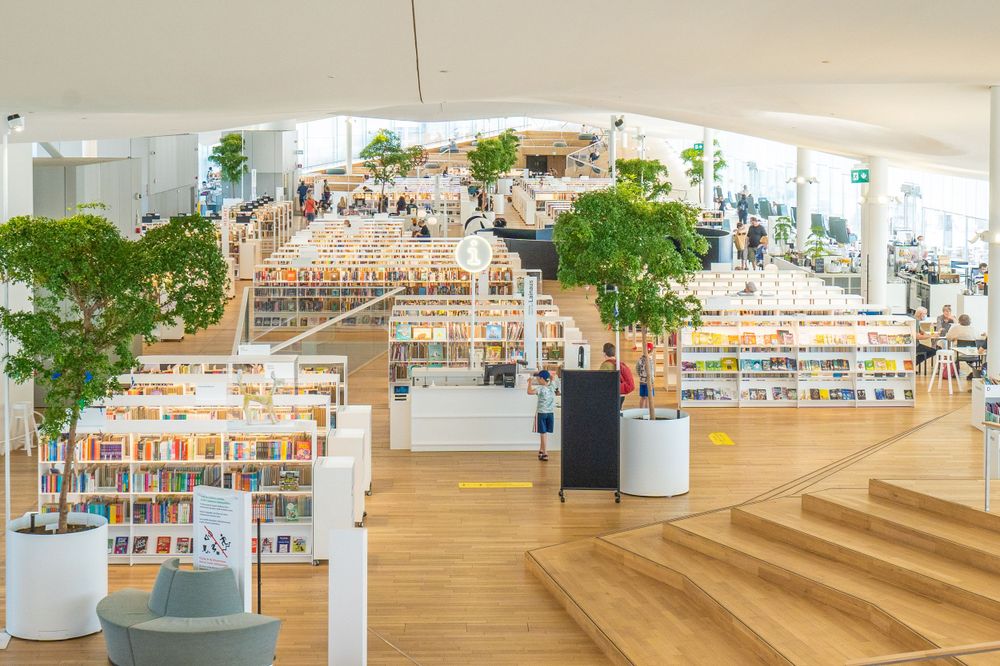 Modern library interior with wooden tiered seating and bookshelves arranged in an open-plan design under natural lighting.