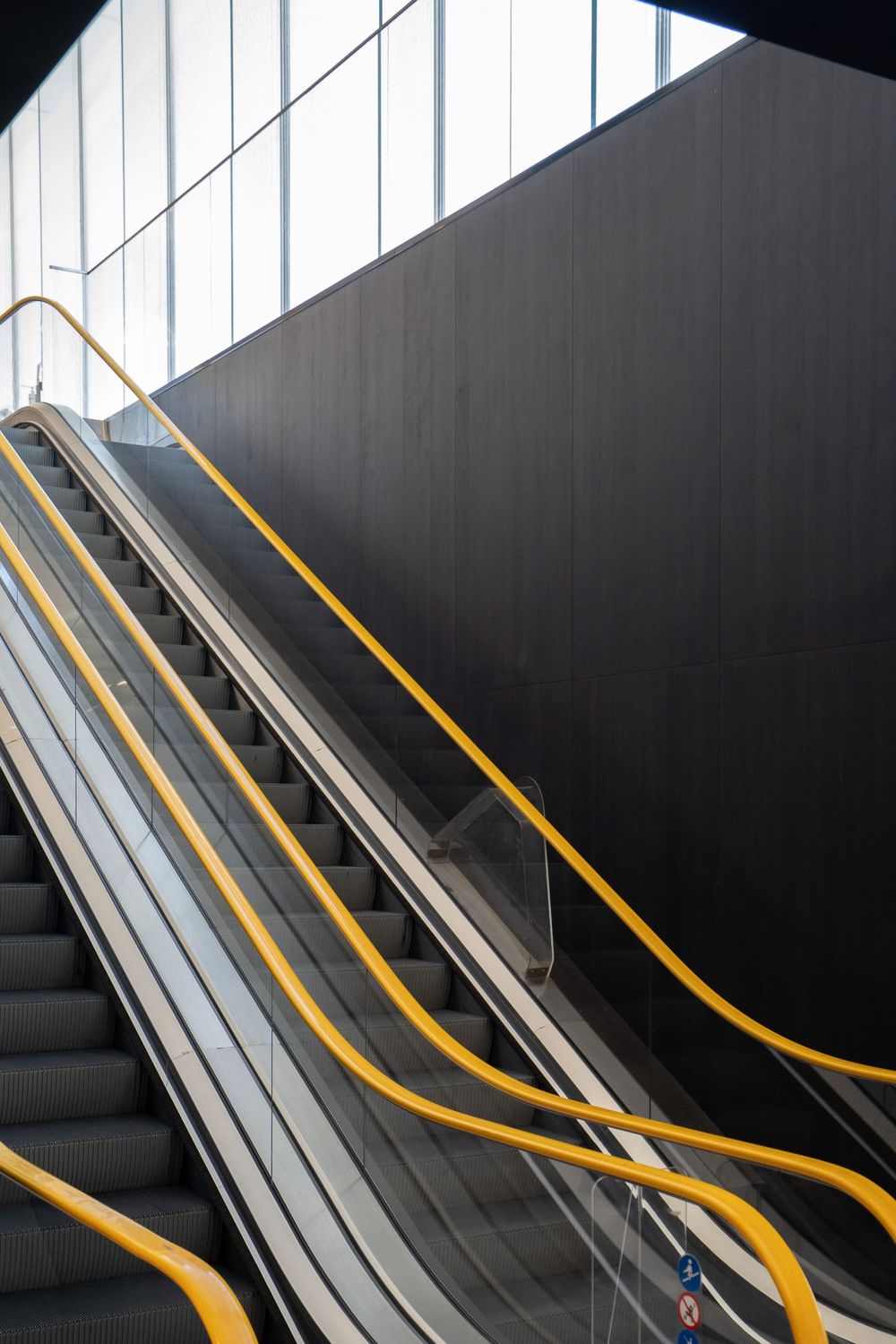 Modern escalator with yellow safety rails against a dark wall in minimalist architectural setting.