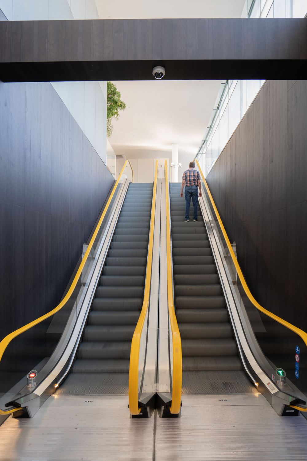 Three parallel escalators with yellow handrails ascending between dark walls in a modern building.