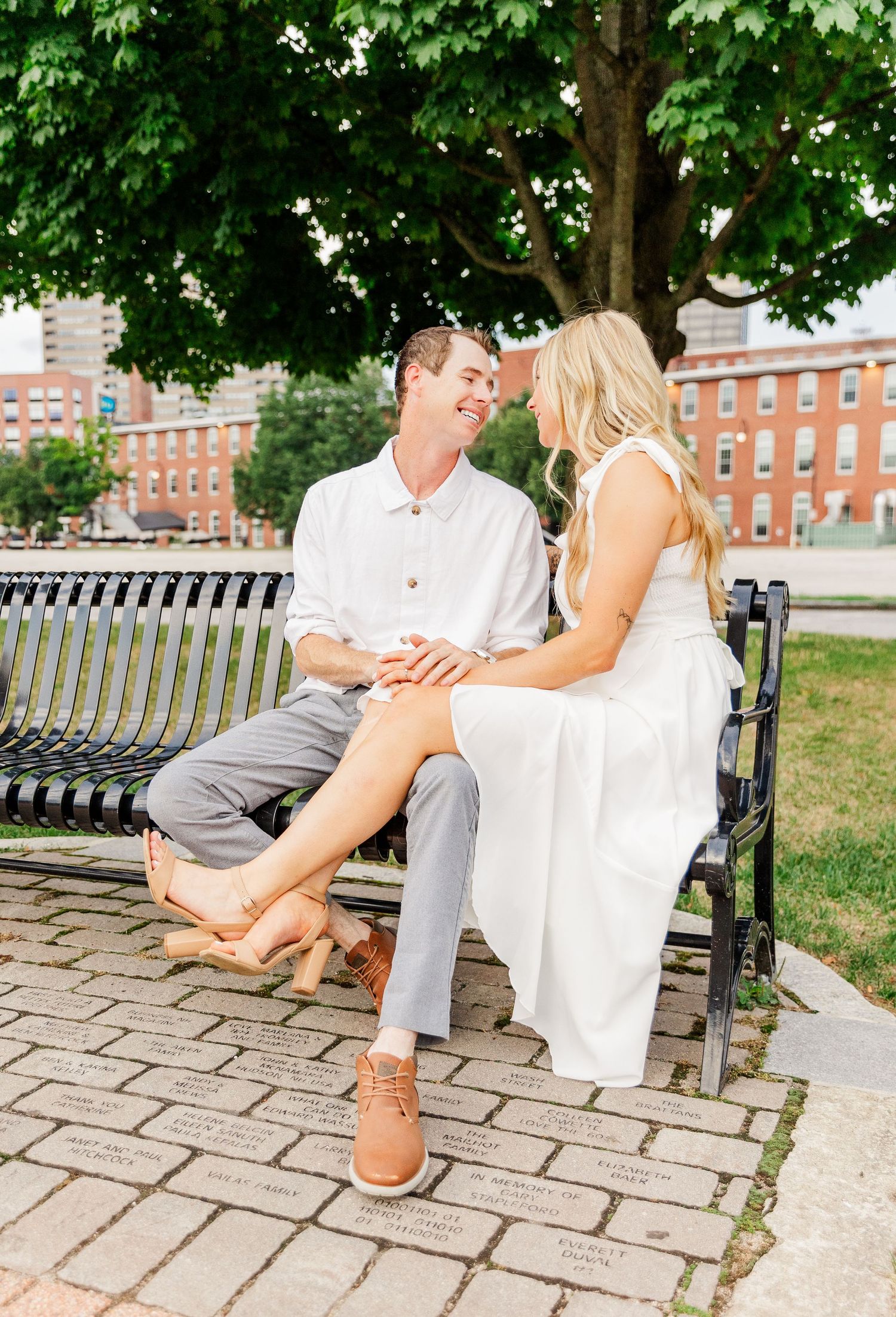 Couple sitting together on park bench under green maple trees.