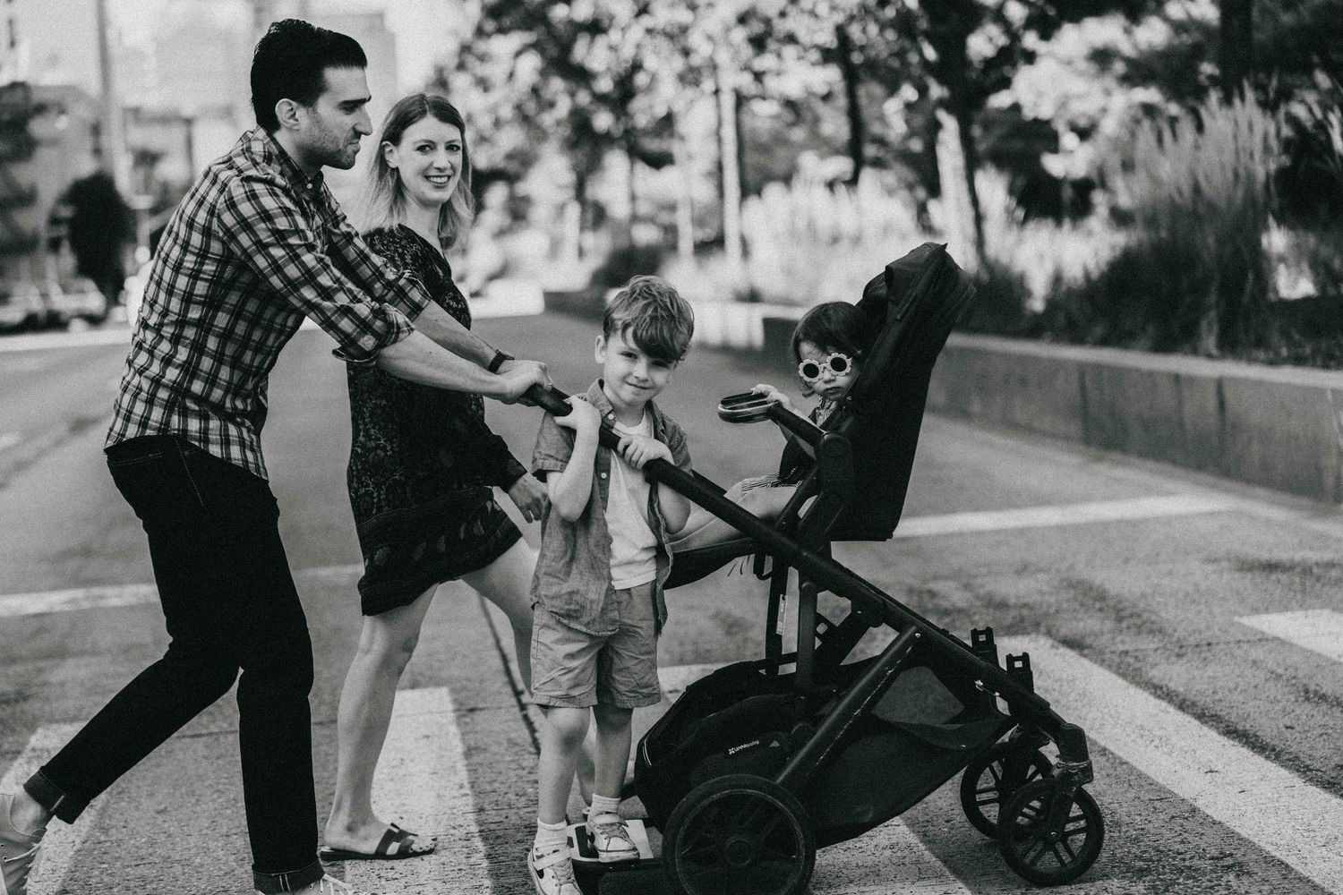 Family having fun together on a sidewalk beside a baby stroller in black and white photography.