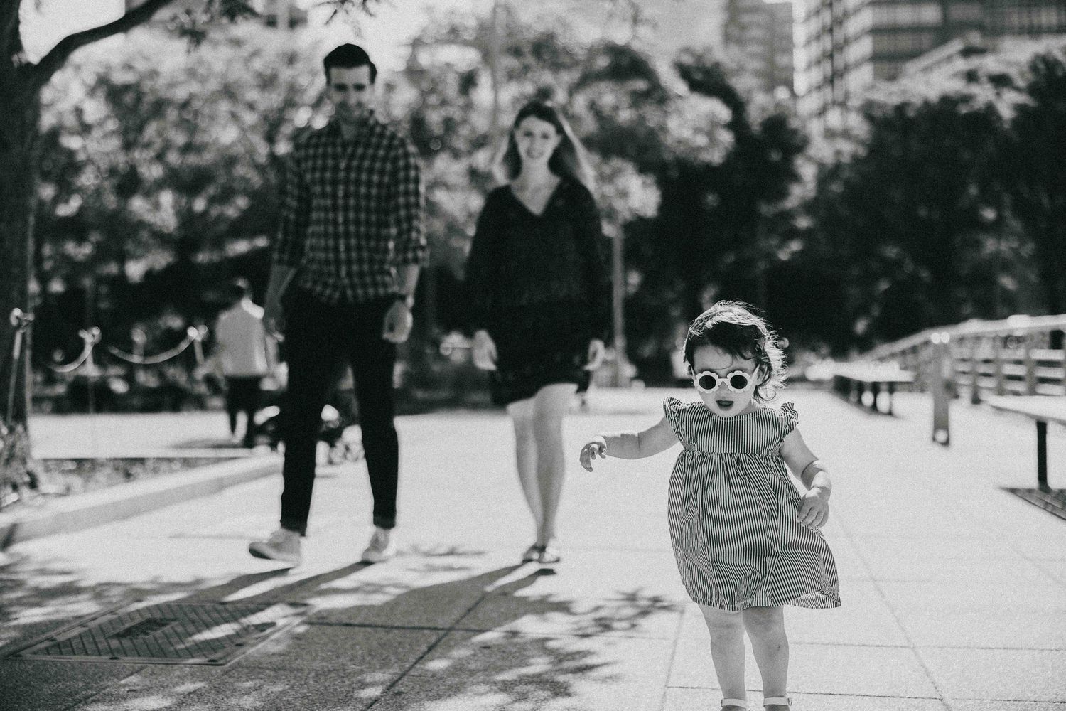 A young child wearing sunglasses runs playfully down a sidewalk in a black and white photograph.