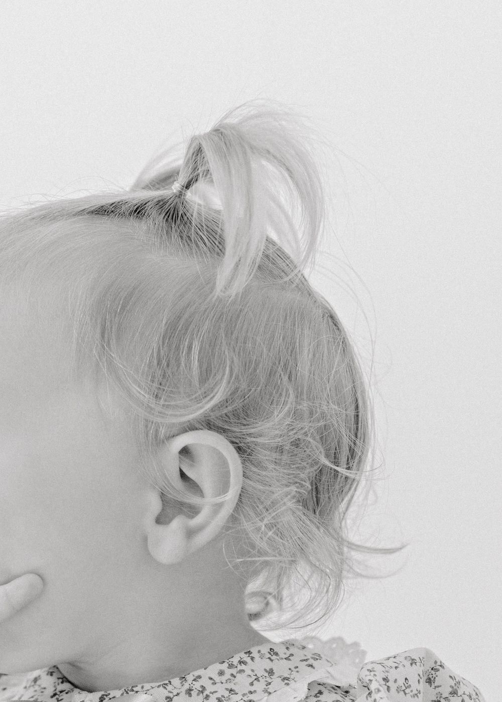 Close-up side view of a small child's ear and wispy blonde hair styled in a messy bun.
