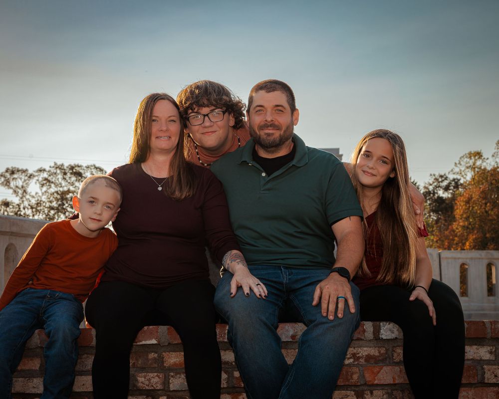 A family of five sits together on a brick wall at sunset during an outdoor portrait session.