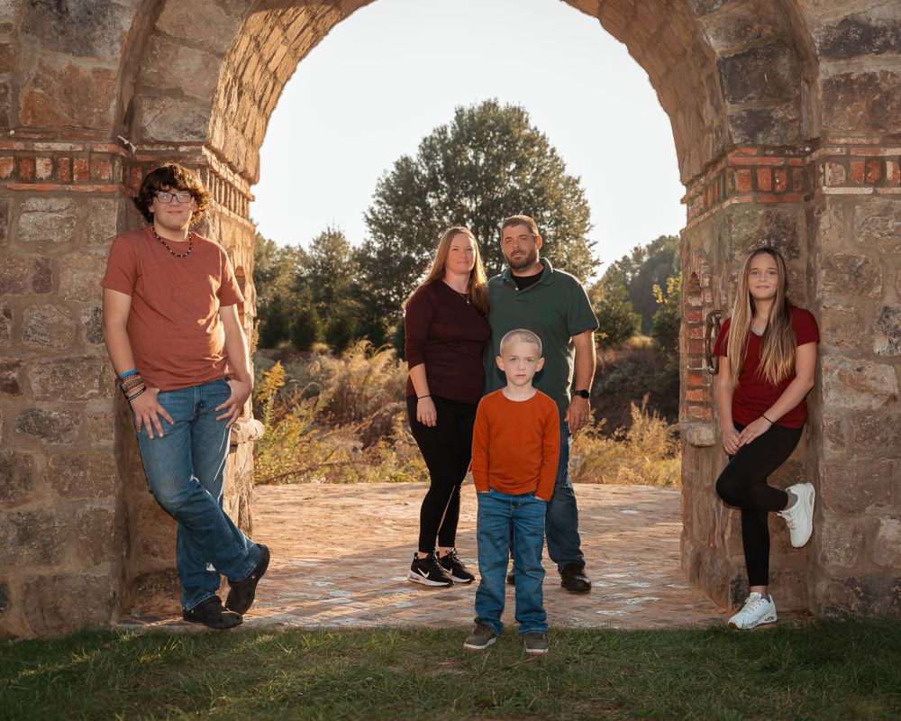 Outdoor family portrait under stone archway with scenic natural landscape in background during golden hour.