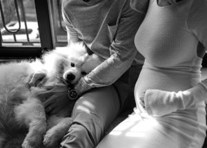 Black and white photo of couple relaxing with their fluffy white dog on couch.