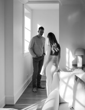 Black and white photo of couple standing in sunlit hallway having intimate conversation.