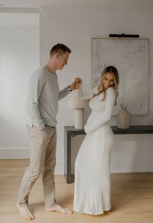 A tender maternity moment captured in a bright room with minimalist decor and natural window lighting.