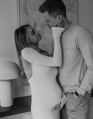 A black and white intimate maternity photo showing a tender moment in a minimalist setting.