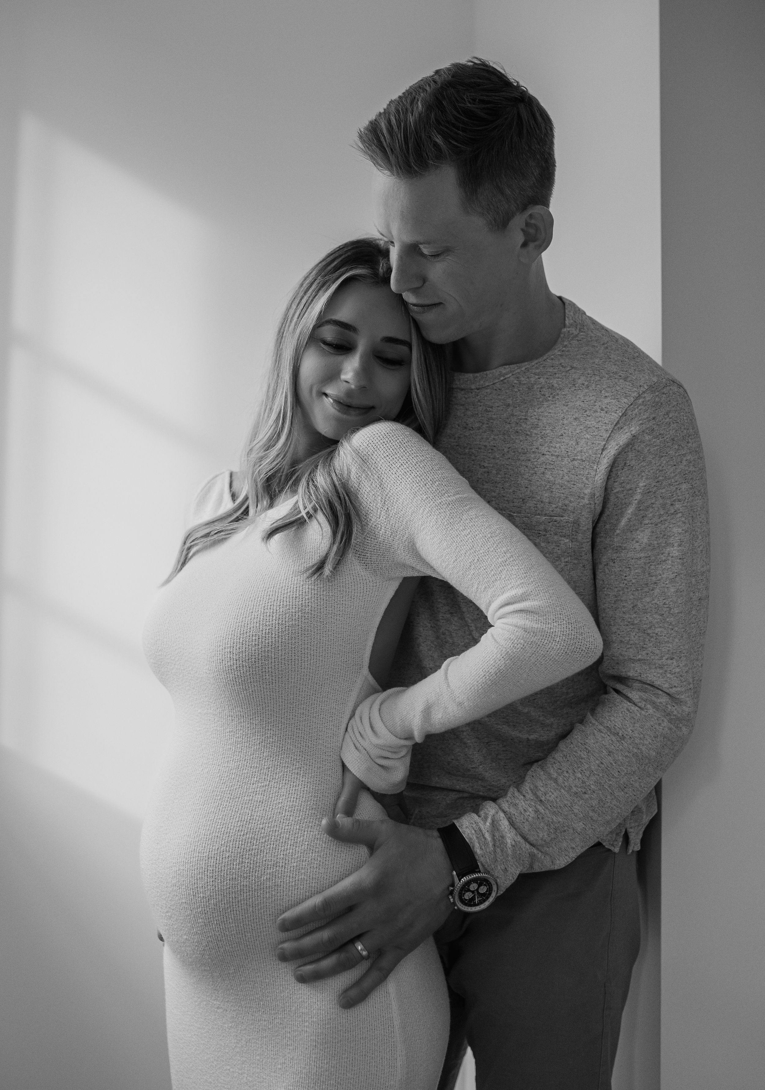 An intimate black and white maternity portrait with soft window light and natural poses.