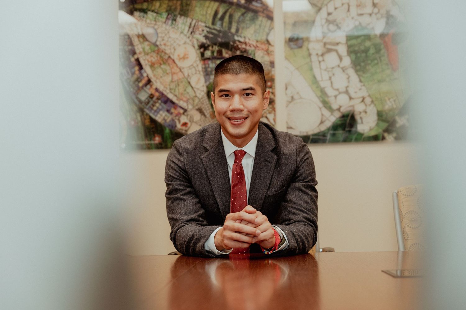 Professional business portrait at wooden conference table with decorative wall art in background.