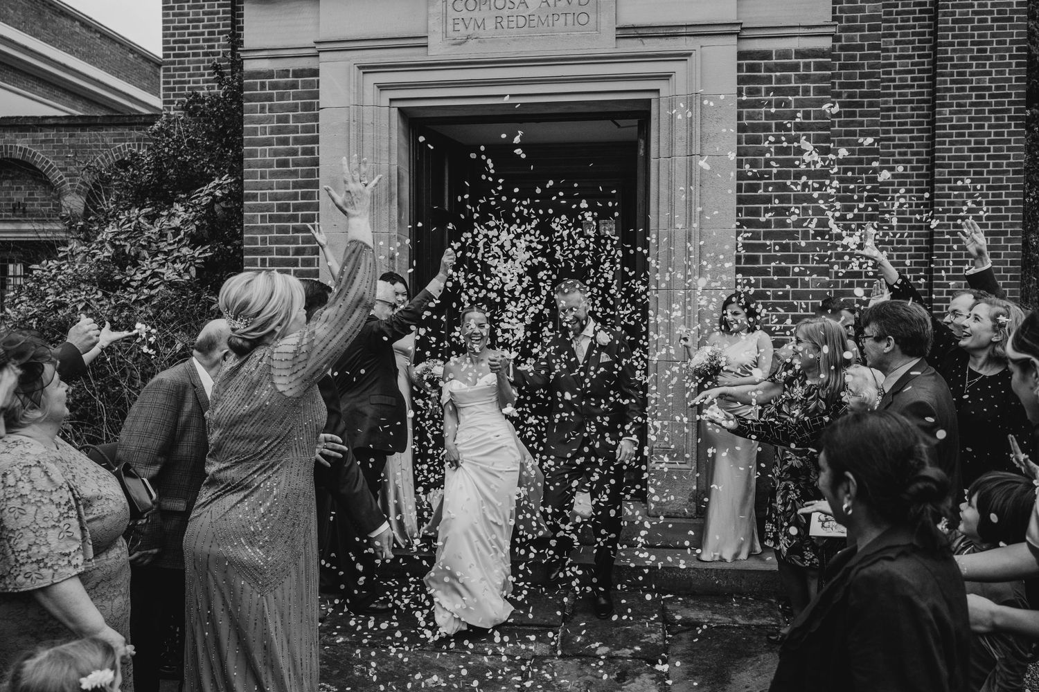 Wedding party celebrating with confetti toss outside church entrance in black and white photography.