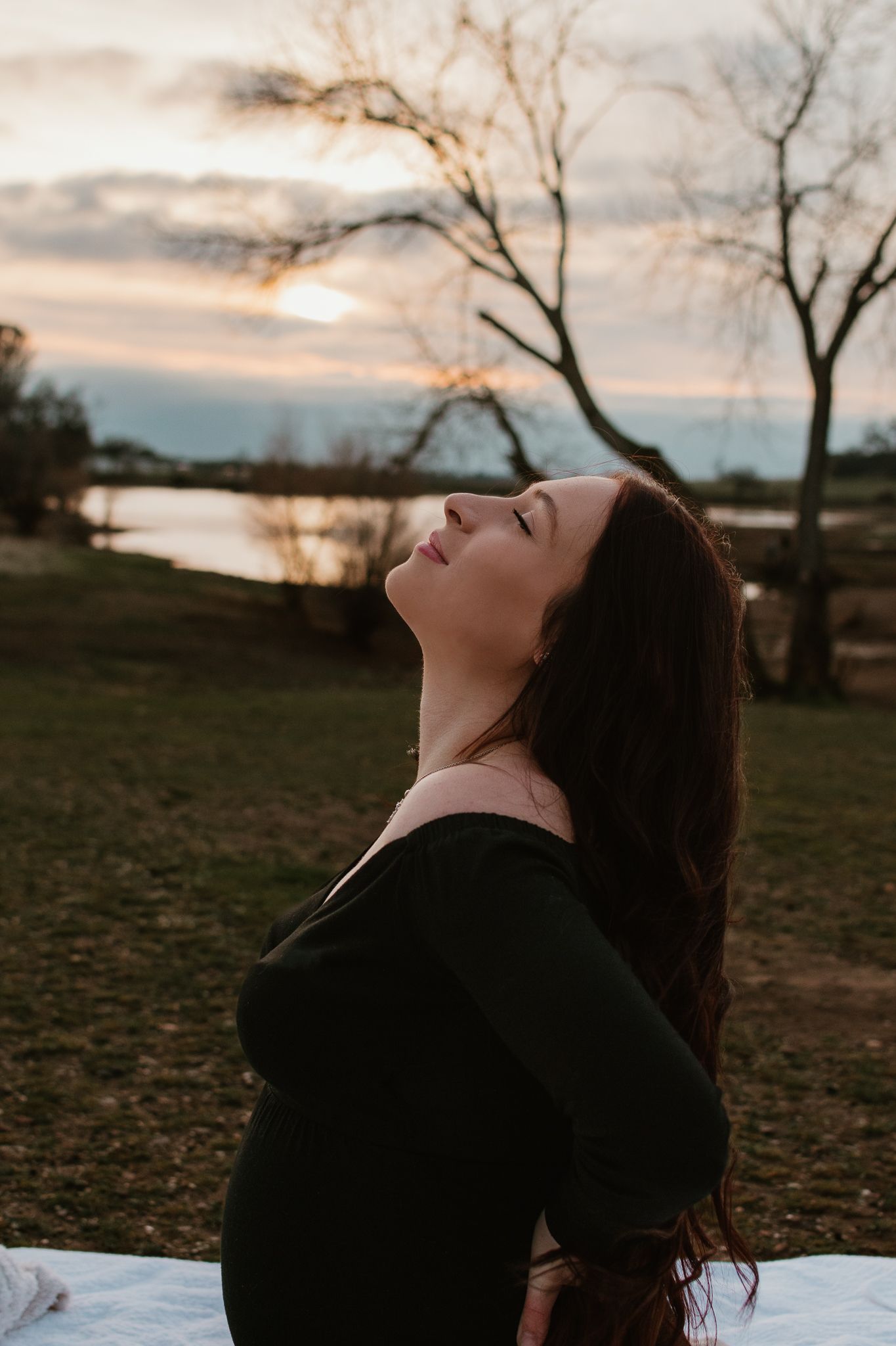Person with long dark hair tilting head back against sunset sky.